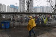 Man wearing a face mask walks past a mural near a construction site n Wuhan