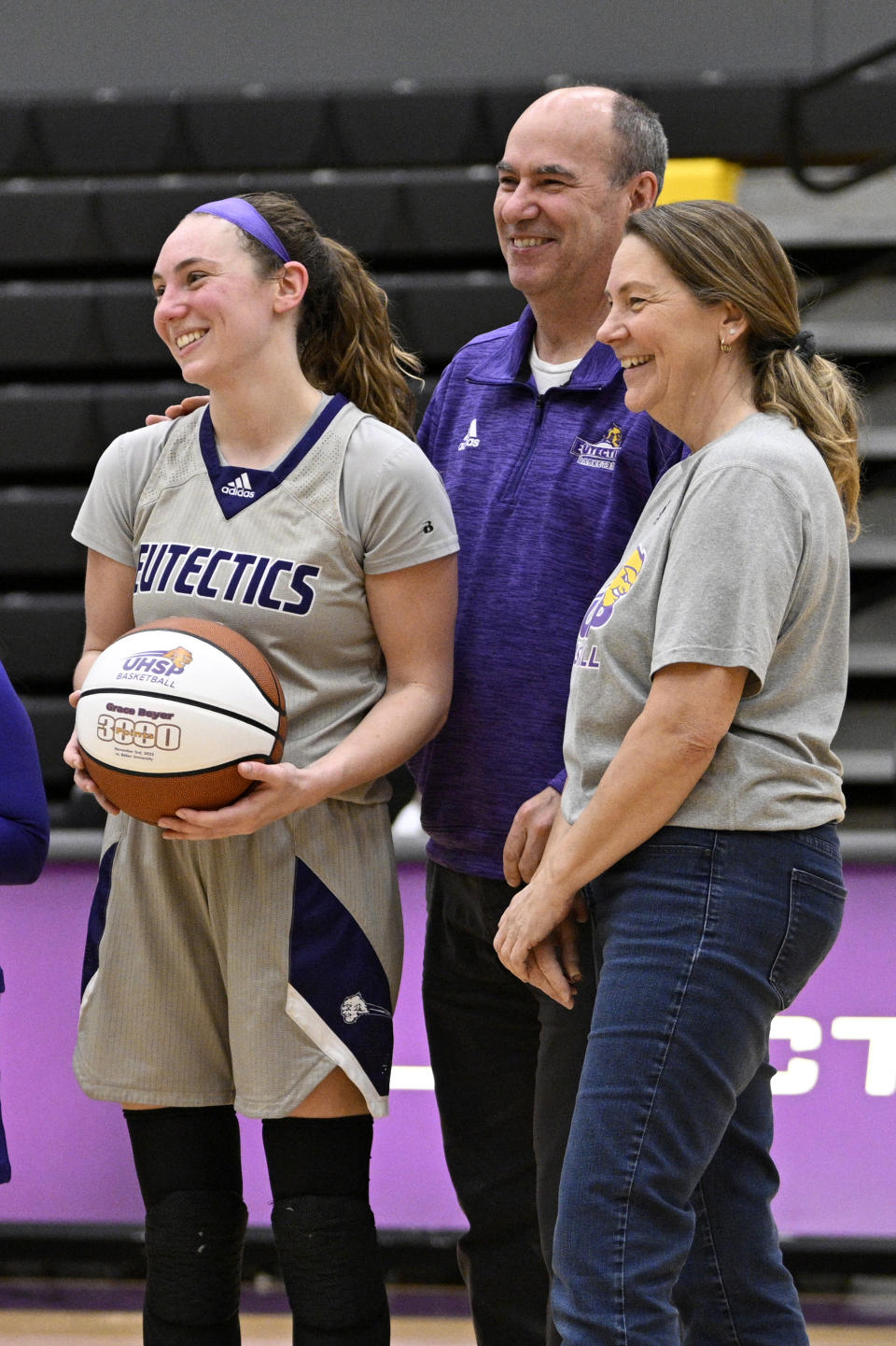 University Health Sciences and Pharmacy Grace Beyer, left, smiles with her parents Bob and Julie right, during a ceremony honoring the guard following an NAIA college basketball game against Cottey College Thursday, Feb. 22, 2024, in St. Louis. The eyes of the sports world have been trained on Iowa star Caitlin Clark's pursuit of women's basketball scoring history, but some have noticed that Grace Beyer at a tiny NAIA school is the only active player with more points than Clark. (AP Photo/Jeff Le)