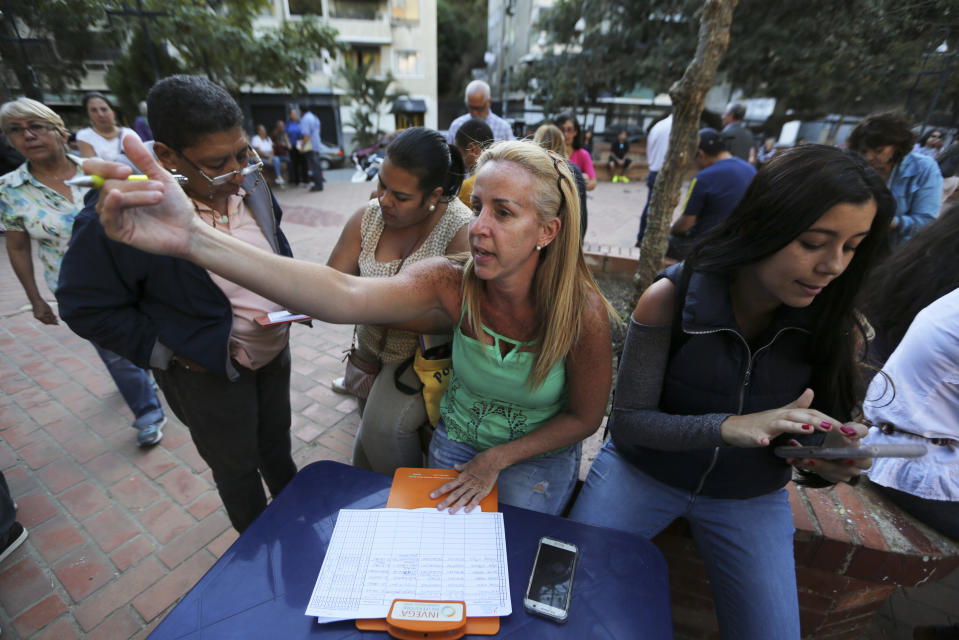 En esta foto del 19 de febrero de 2019, la gente llena formatos para unirse al grupo de voluntarios que ayudará a introducir ayuda humanitaria a Venezuela en una plaza de Caracas, Venezuela. (AP Foto/Fernando Llano)