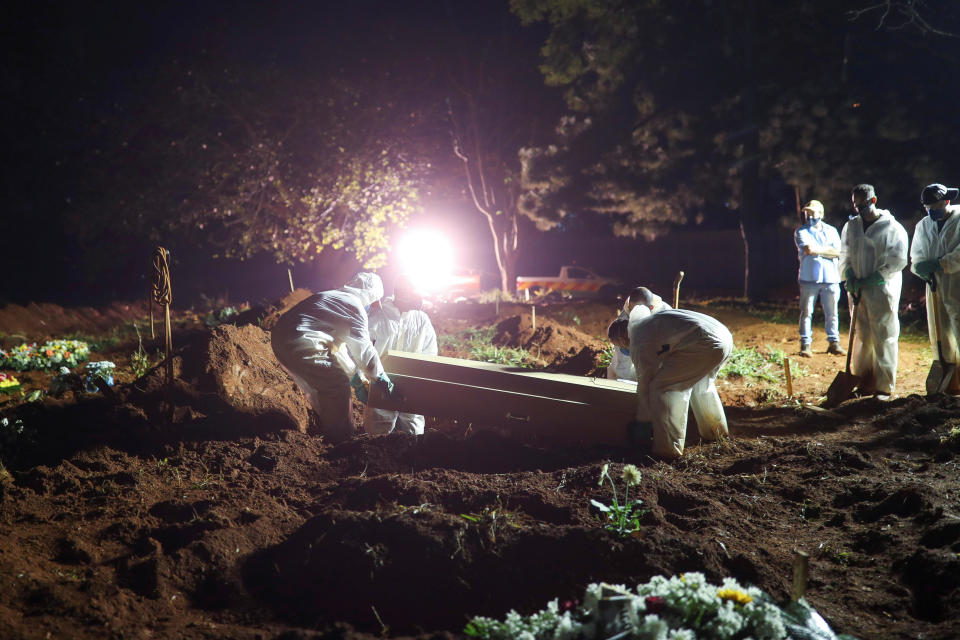 Gravediggers wearing protective suits carry the coffin of a 32-year-old man who died from the coronavirus disease (COVID-19) as spotlights illuminate the graves during night burials at Vila Formosa cemetery in Sao Paulo, Brazil, March 30, 2021. / Credit: AMANDA PEROBELLI/REUTERS