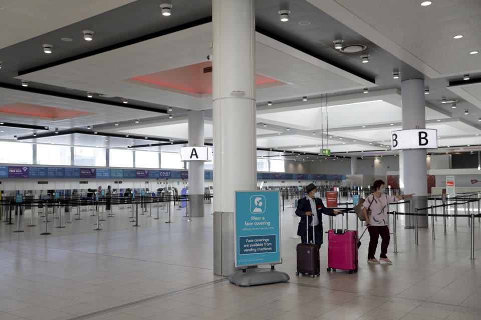 Passengers walk past a coronavirus face coverings sign at the North Terminal of Gatwick Airport near Crawley, just south of London, Wednesday, July 22, 2020. With all schools now closed, Friday would normally be the busiest departure day of the year for London’s Gatwick Airport with families heading off to the sun-soaked beaches in southern Europe. Not this year as the coronavirus pandemic has meant many have opted against making their annual summer migration to countries like Spain and Greece. Gatwick would in any normal year be expecting to fly some 85,000 holidaymakers on Friday alone. It expects less than 10,000 passenger departures on Friday. (AP Photo/Matt Dunham)