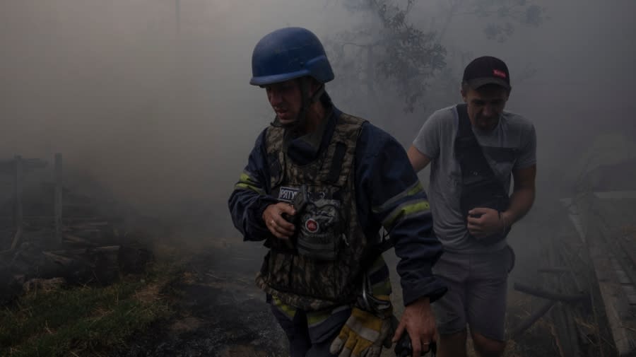 <em>A firefighter walks with of a resident through smoke coming from a house on fire, after cluster rockets hit a residential area, in Konstantinovka, eastern Ukraine, on Saturday, July 9, 2022. (AP Photo/Nariman El-Mofty)</em>