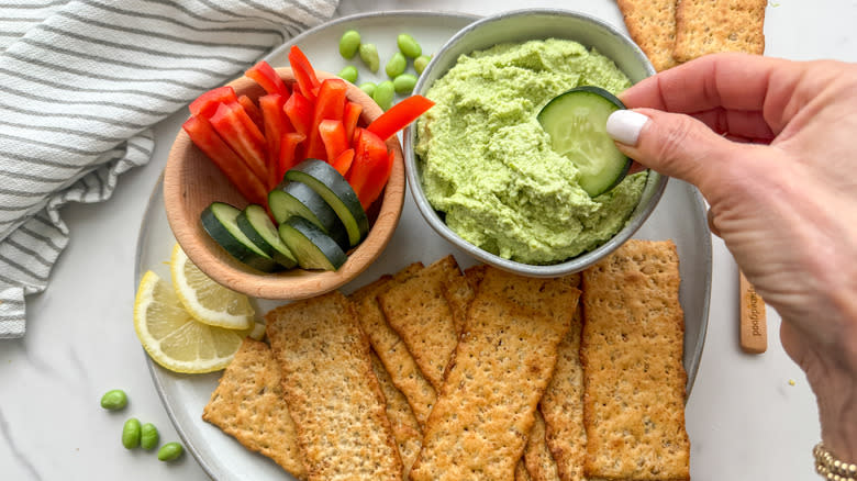 hand dipping cucumber in hummus