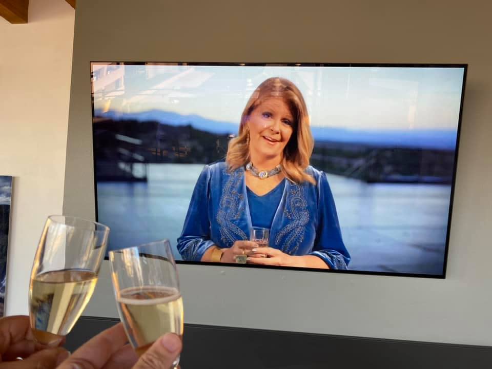 This July 3, 2020 image provided by Peter Batty shows him and his wife toasting as they celebrate their anniversary and watch mezzo-soprano Susan Graham host opening night of the Santa Fe Opera on their television in Denver, Colorado. The famed opera is offering a series of virtual performances after being forced to cancel the 2020 season due to the coronavirus pandemic. The Saturday night events are meant to celebrate the five originally-scheduled operas that would have been performed this summer. (Peter Batty via AP)