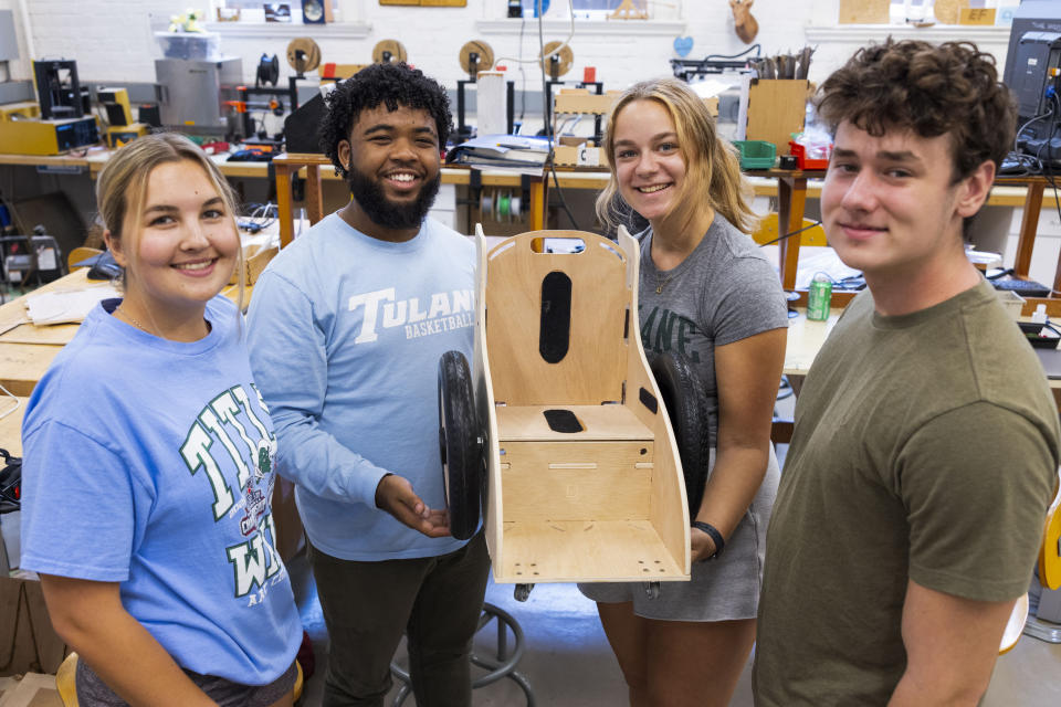 This photo released by Tulane University shows students, left to right, Kailee Oswald, Shayne Shelton, Leah Abraham and Solomon Lissauer, showing of a finished product as they build the specially designed chairs for children at the MakerSpace workshop at the university Sunday, Sept. 24, 2023. The students are making the second batch of mobility chairs for toddlers, that will eventually go to pediatric patients at Children's Hospital. Wheelchairs are expensive, and insurance won't cover the cost for children unless the child proves they can operate it independently. (Sabree Hill/Tulane University via AP)