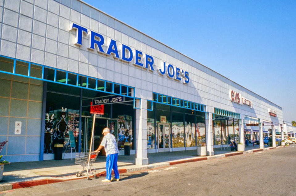 A person pushing a cart towards the entrance of a Trader Joe's that's next to a CVS