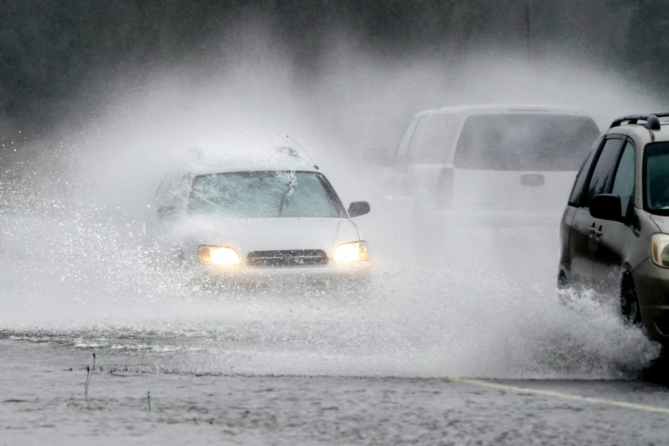 A westbound car is caught in a spray of water thrown up by a pickup truck on Highway 20 Monday, Nov. 15, 2021, near Hamilton, Wash. The heavy rainfall of recent days will brought major flooding of the Skagit River that is expected to continue into at least Monday evening. (AP Photo/Elaine Thompson)