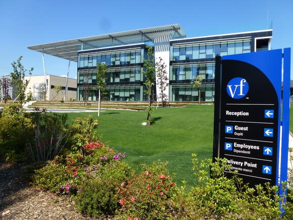 Glass-walled three-story building with grass lawn, flowers, and VF sign directing traffic to various parking lots.