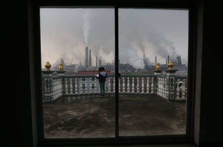 A girl reads a book on her balcony as smoke rises from chimneys of a steel plant, on a hazy day in Quzhou, Zhejiang province in this April 3, 2014 file photo. REUTERS/Stringer