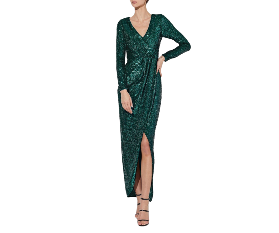 A caucasian woman with her head cropped out of the image wears a long sleeve emerald green sequin dress with black strappy heels against a white background. 