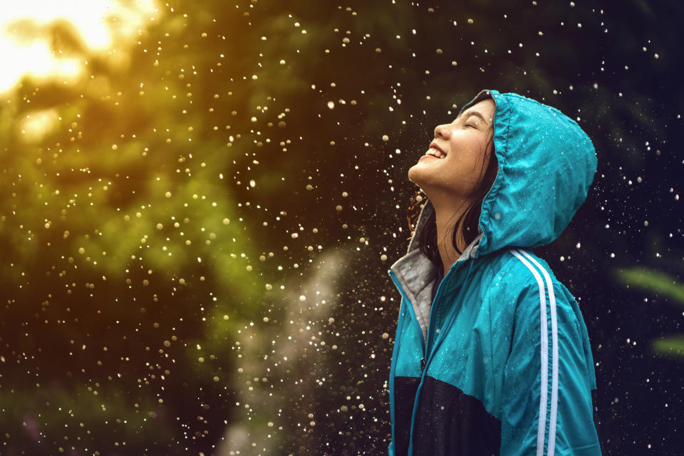 A woman smiling and looking up at the rain