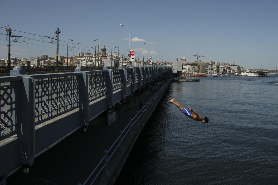 Backdropped by Galata Tower, a youth jumps from the Galata Bridge into the Golden Horn leading to the Bosphorus Strait separating Europe and Asia, in Istanbul, Friday, May 14, 2021. Turkey is in the final days of a full coronavirus lockdown and the government has ordered people to stay home and businesses to close amid a huge surge in new daily infections. But millions of workers are exempt and so are foreign tourists. Turkey is courting international tourists during an economic downturn and needs the foreign currencies that tourism brings to help the economy as the Turkish lira continues to sink. (AP Photo/Emrah Gurel)