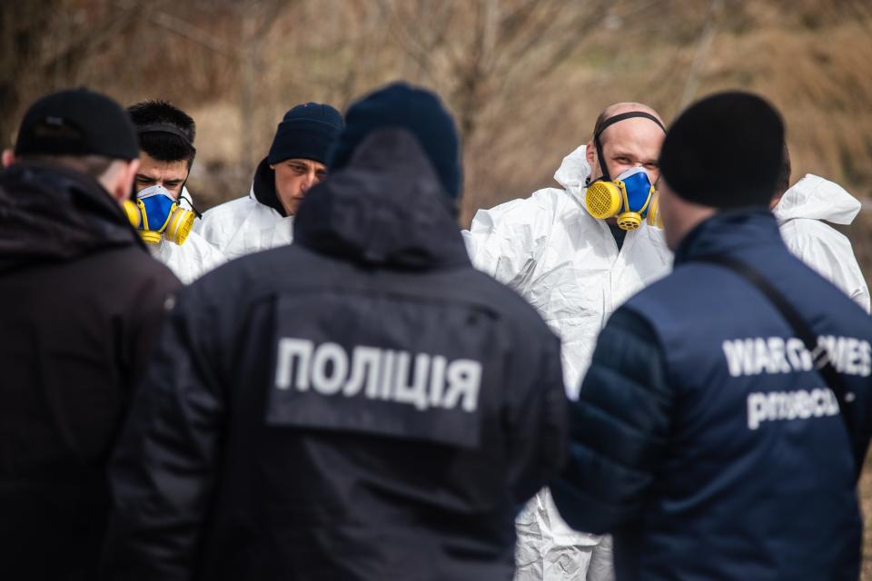 Man in navy coats and white coats face one other, with some wearing gas masks.