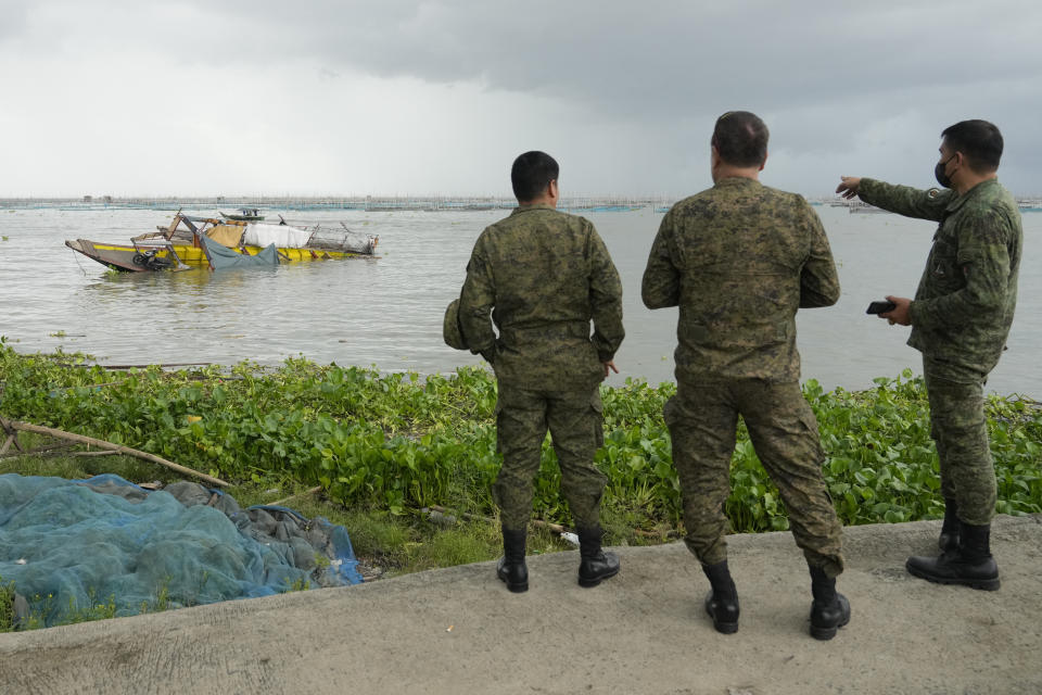 Military men look at a passenger boat that capsized in Binangonan, Rizal province, Philippines on Friday, July 28, 2023. The small Philippine ferry turned upside down when passengers suddenly crowded to one side in panic as fierce winds pummeled the wooden vessel, leaving scores of people dead while others were rescued, officials said Friday. (AP Photo/Aaron Favila)