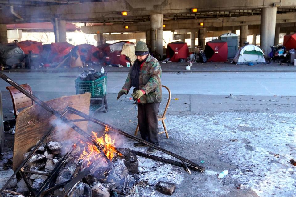 PHOTO: An elderly man warms his hands by the fire he created across the street from a homeless encampment under a major interstate freeway, Jan. 16, 2024, in Chicago. (Charles Rex Arbogast/AP)