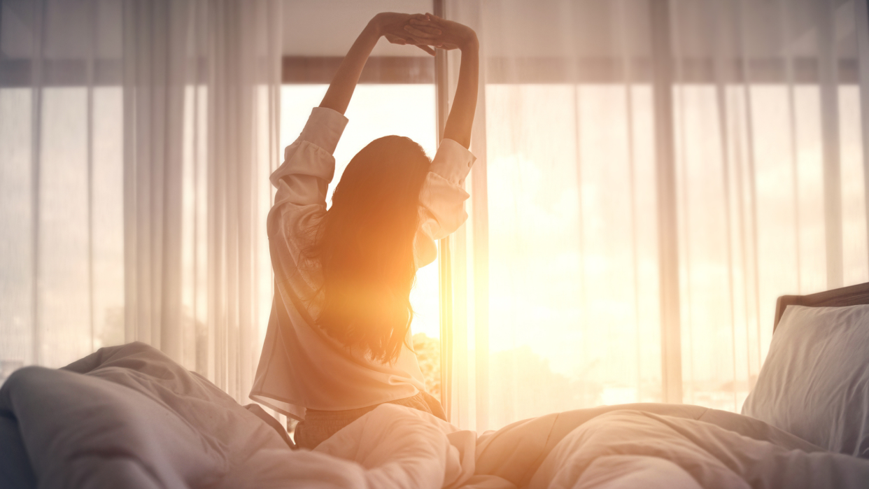  Woman stretches as she gets out of bed in front of the sunrise. 