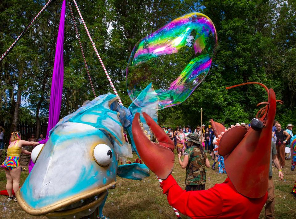 A performer dressed as a lobster reaches for a soap bubble floating over the crowd as she joins the group Primordial Soup at the Oregon Country Fair for 2022.