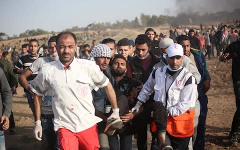 Palestinians carry a wounded man during the protests at the Gaza border - Credit: Getty