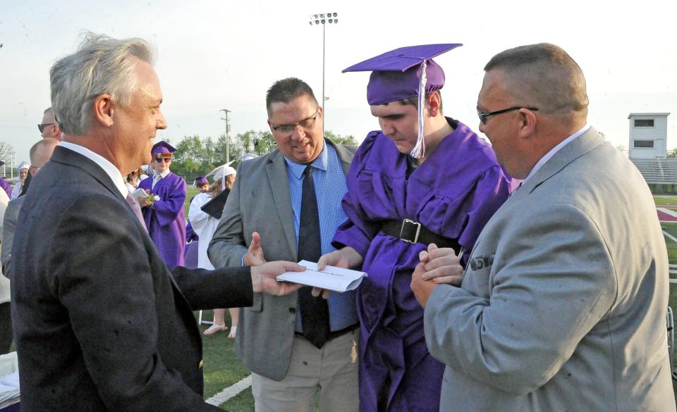 With support by Brian Kiper and Pat Honza, Christian Mendoza receives his diploma from Triway school board member Donald Noble.