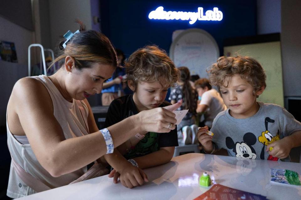 Jayme Eglin, left, shows her sons Eli, center, and Archer, how they will hold her pinhole cameras in the shadow to see the solar eclipse on Monday, April 8, 2024, at The Phillip and Patricia Frost Museum of Science in downtown Miami.