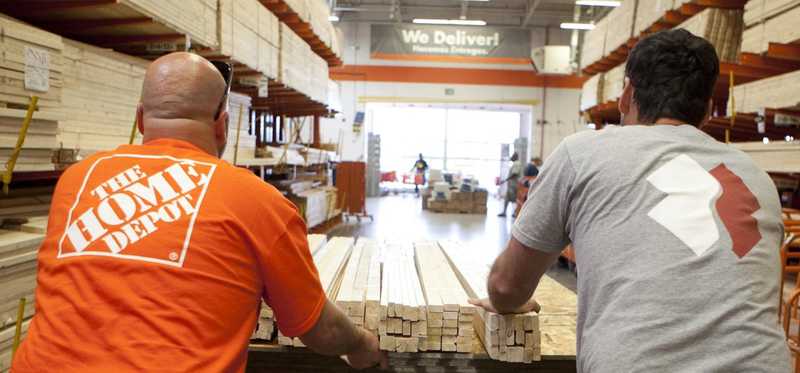 two men pushing cart of wood down an aisle in Home Depot store