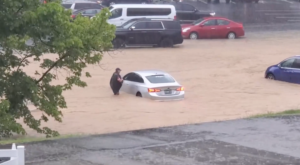 A person stands in waist-deep water next to a submerged car at Dollywood in Pigeon Forge, Tennessee as heavy rain causes flash flooding throughout the amusement park (TMX)