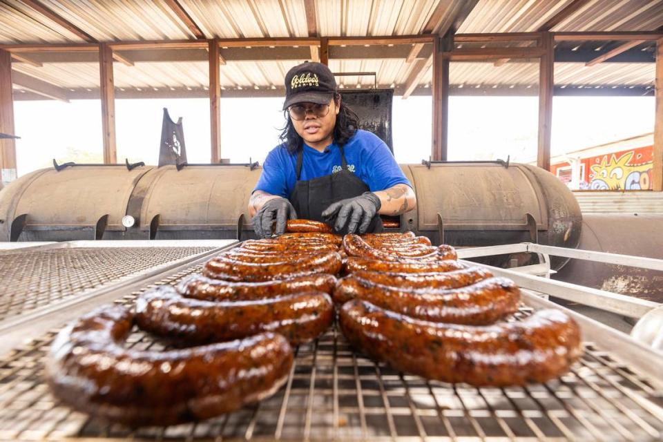 Nupohn Inthanousay, copropietario de Goldee's Barbecue, saca la salchicha ahumada de Laos del ahumador y la coloca en rejillas para enfriar en Goldee's antes del servicio en Fort Worth el viernes 28 de junio de 2024.