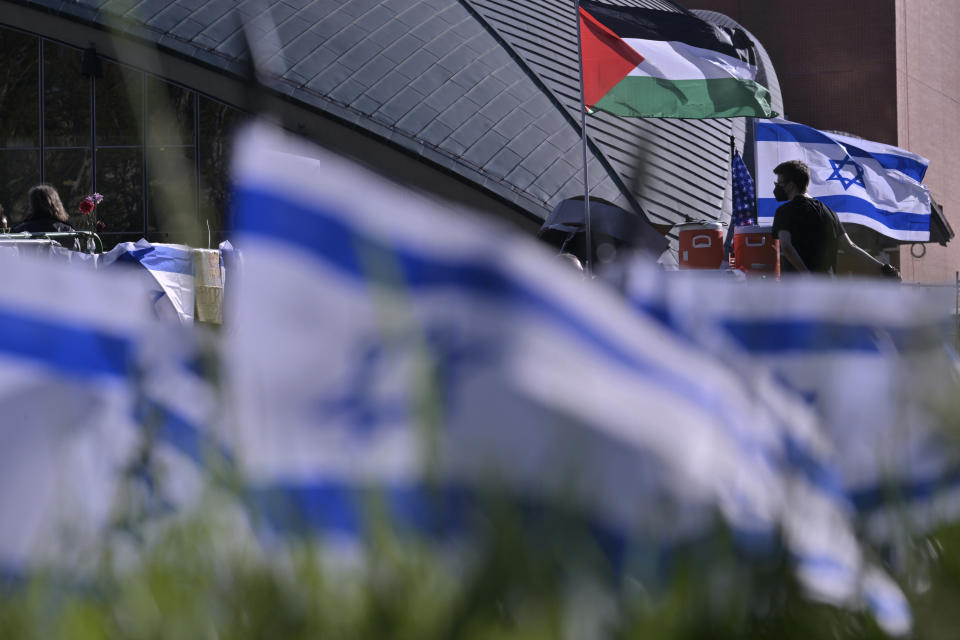 A man walks below flags at a Pro-Palestinian encampment at MIT, Thursday, May 9, 2024, in Cambridge, Mass. MIT has suspended 23 students for participating in the encampment, and police detained at least three during a demonstration at the nearby Stata center, where demonstrators blocked traffic over claims the university was conducting research which would be used for Israeli military drones. (AP Photo/Josh Reynolds)