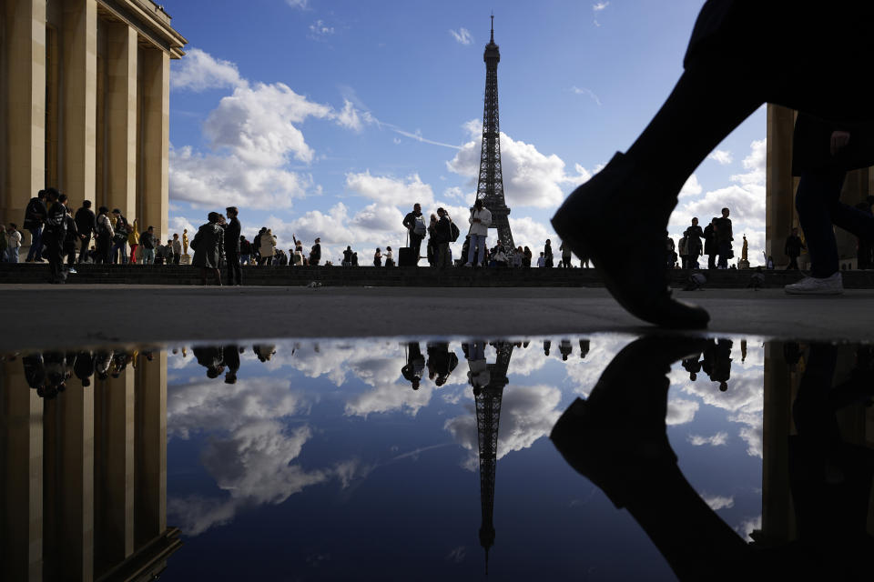 The Eiffel Tower is reflected in a puddle as people walk past at the Trocadero square, in Paris, France, Tuesday, Oct. 24, 2023. (AP Photo/Pavel Golovkin)
