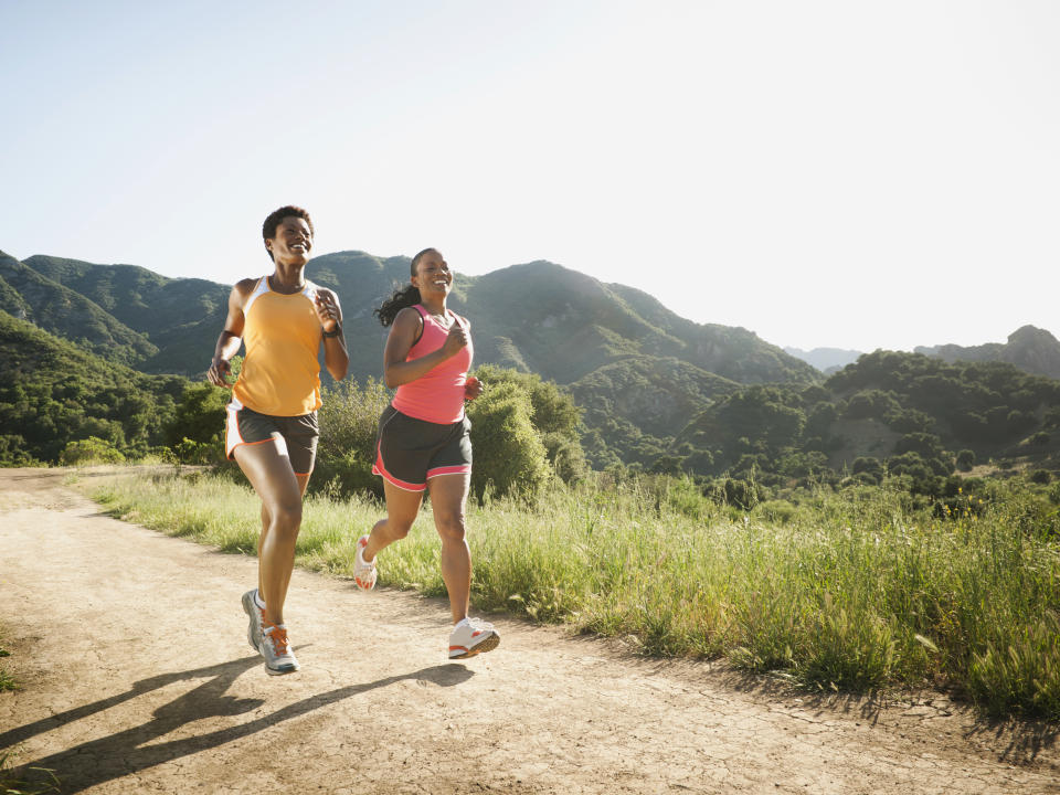 Two women jogging on a trail with scenic mountains in the background