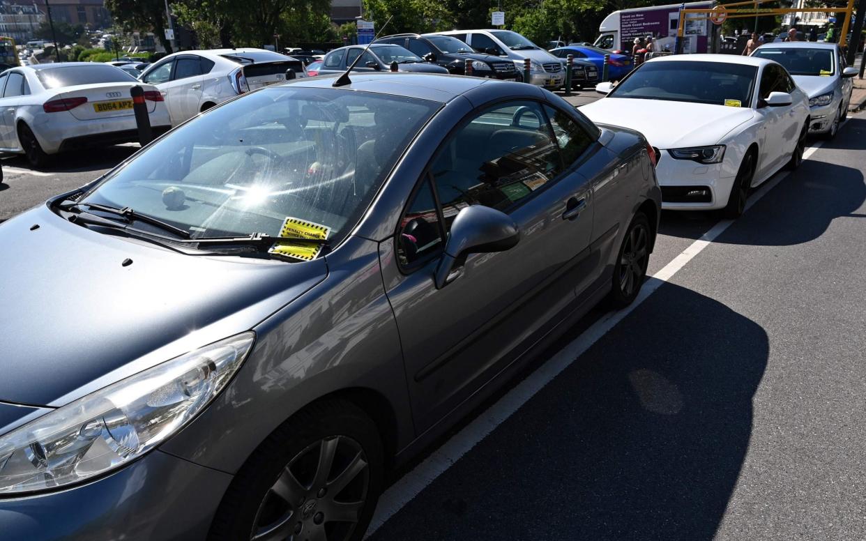 Yellow parking tickets are pictured on the windscreens of cars - Glyn Kirk/AFP