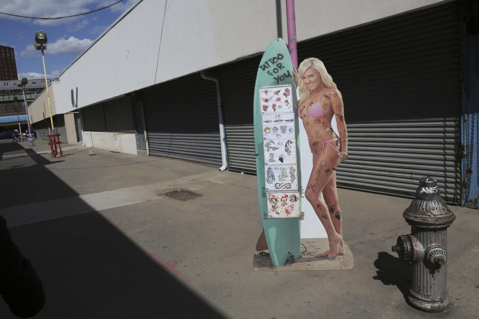 In a Saturday March 30, 2013, photo a life size poster of a model advertising a temporary tattoo shop is framed by shuttered businesses at New York's Coney Island. Despite making the traditional Palm Sunday opening, many of the seasonal businesses at Coney Island are still reeling from the aftermath of Superstorm Sandy. (AP Photo/Mary Altaffer)