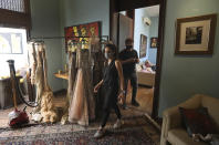 Back stage staff wearing face masks walk past a room where outfits are hung for a shoot ahead of the Lotus Make-up India Fashion Week, in the farmhouse of the designer in New Delhi, India, Friday, Oct. 2, 2020. Unlike a fashion show, they aren't swaying live on a ramp. They are depending on digital technology to rescue their annual extravaganza from the coronavirus pandemic with ''Phygital edition." India’s first digital fashion week is being held from Oct. 14-18, live streaming the spring-summer collections by more than 40 fashion designers. (AP Photo/Manish Swarup)