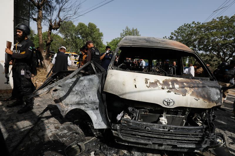 Police officers and members of the investigation team gather near a passenger van, after a blast at the entrance of the Confucius Institute University of Karachi