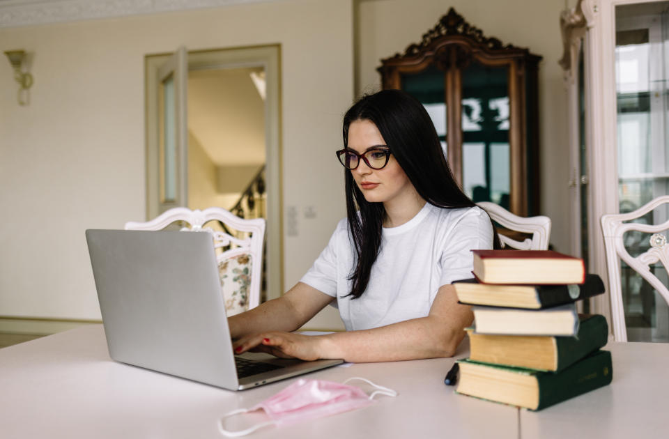 a girl sitting with her laptop, books, and a mask