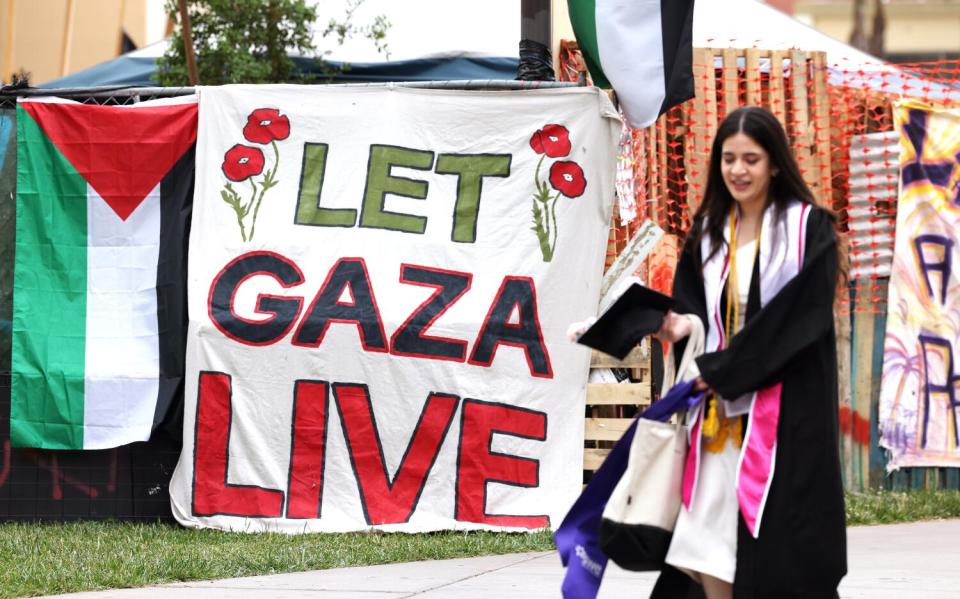 A student wearing a graduation gown passes a banner that says, "Let Gaza Live."