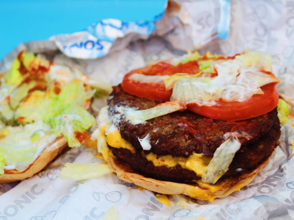 open faced sonic double cheeseburger in tin foil wrapping on blue background