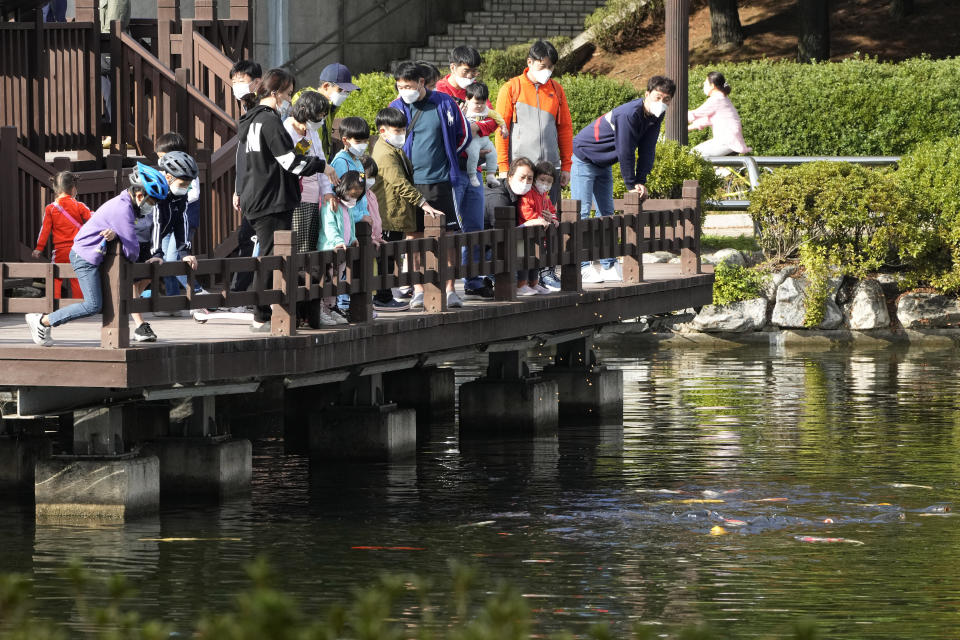 People wearing face masks as a precaution against the coronavirus feed fish at a park in Goyang, South Korea, Monday, Oct. 11, 2021. (AP Photo/Ahn Young-joon)