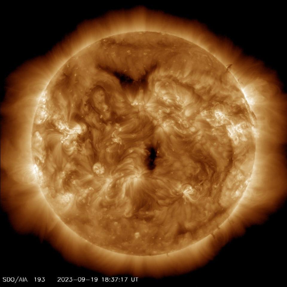 the sun glowing yellow-orange orb in black space covered in roiling plasma with two dark large spots