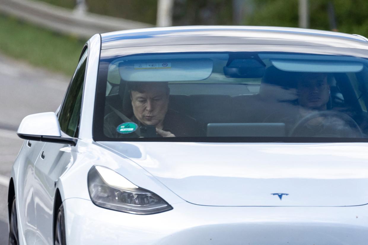 Tesla CEO Elon Musk (L) is seen as he uses his mobile device in the car arriving to the construction site for the new plant, the so-called 