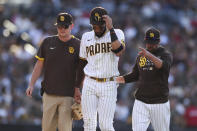 San Diego Padres shortstop Fernando Tatis Jr., center, walks off the field with manager Jayce Tingler, right, after diving for a ball in the fifth inning of a baseball game against the Cincinnati Reds, Saturday, June 19, 2021, in San Diego. (AP Photo/Derrick Tuskan)