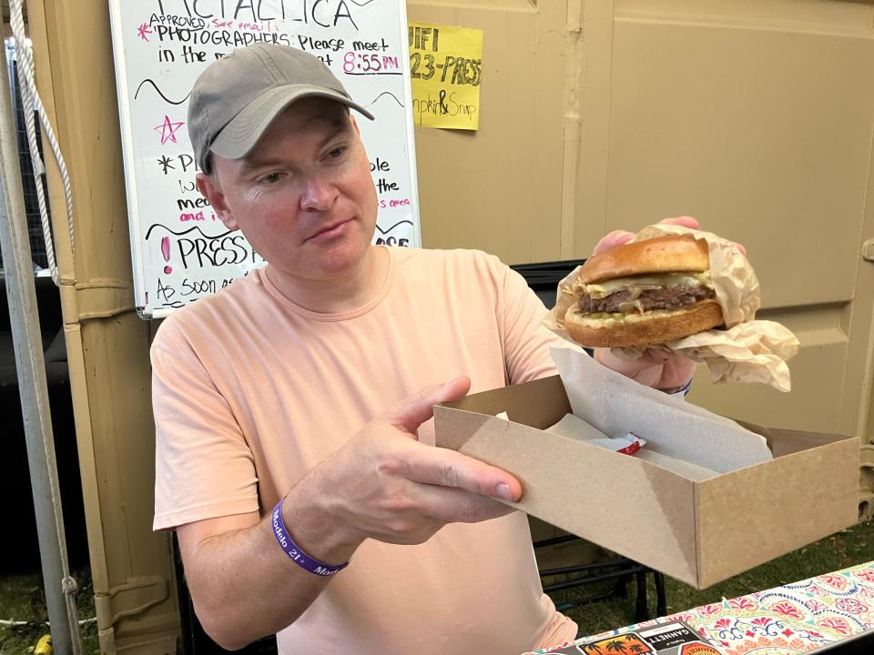 Desert Sun reporter Andrew John shows off his AC/DC burger from Grill 'Em All, a food vendor at Power Trip music festival that offers three heavy metal-themed burger options at the Empire Polo Club in Indio, Calif., Sunday, Oct. 8, 2023.