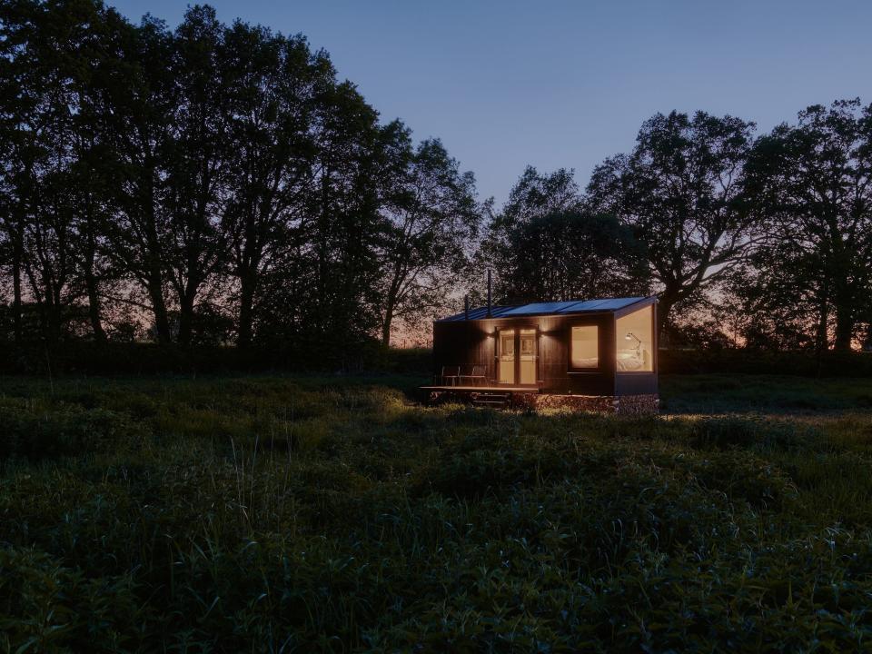 A Raus cabin in nature surrounded by trees and open fields at night.