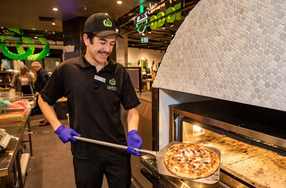 A Woolworths supermarket worker holds pizza fresh out of the oven. 