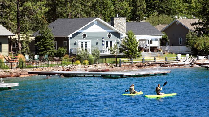 Bigfork,Montana,USA - August 18,2019: Two young people,male and female on paddle boards in front of modern waterfront homes.