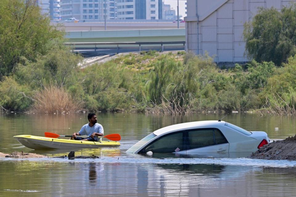 A man steers his canoe past a stranded car on a flooded street in Dubai following heavy rains (AFP via Getty Images)