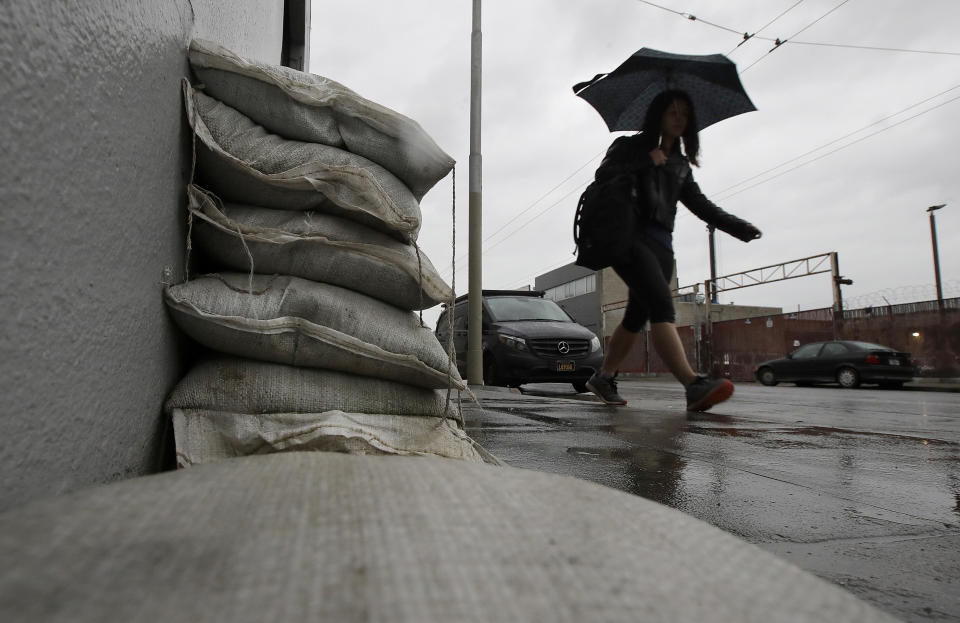 A woman walks past sand bags blocking an entry to a business in San Francisco, Friday, Feb. 1, 2019. A powerful storm bearing down on California on Friday was expected to produce heavy rainfall, damaging winds, localized stream flooding and heavy snow in the Sierra Nevada, forecasters said. (AP Photo/Jeff Chiu)