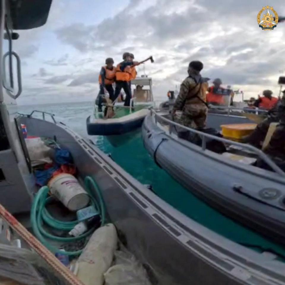 In this photo provided by the Philippine military, Chinese coast guards hold an axe as they approach Filipino troops in the Second Thomas Shoal