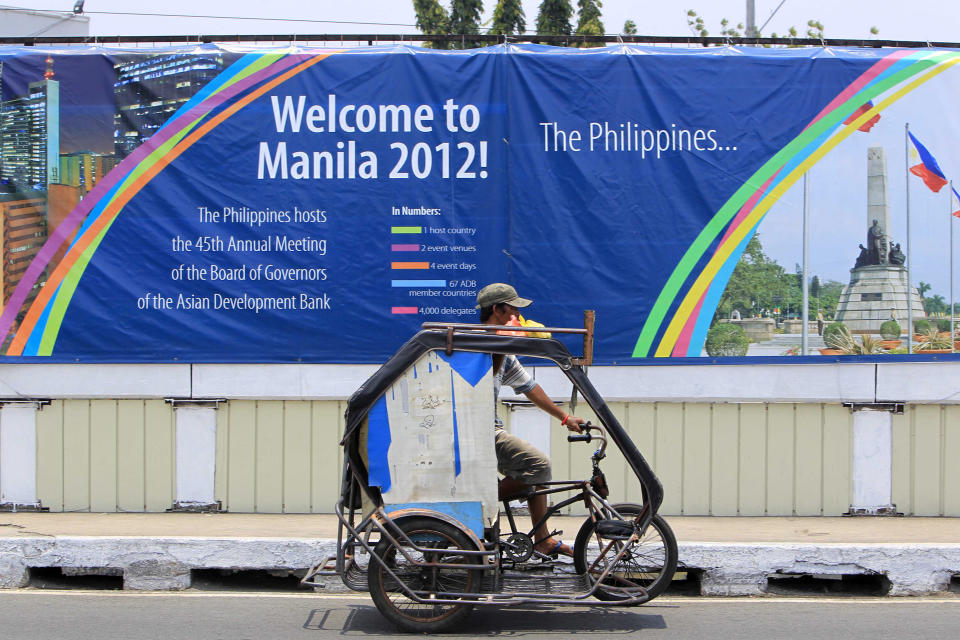 A resident pedals his tricycle, locally known as "pedicab", past a wall covered with a tarpaulin poster of the ongoing 45th Annual Board of Governors meeting of the Asian Development Bank at suburban Pasay city south of Manila, Philippines, Thursday May 3, 2012. Delegates attending the international conference of the ADB in the Philippines capital may not see what they came to discuss: abject poverty. The makeshift, temporary wall on both sides of the bridge from the airport to downtown Manila, hides a sprawling slum along a garbage-strewn creek. (AP Photo/Bullit Marquez)