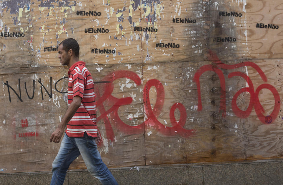 In this Oct. 17, 2018 photo, a man walks past graffiti that reads in Portuguese: "Not him" in Rio de Janeiro, Brazil. Polls have consistently shown that both candidates for the presidency have the highest rates of rejection, defined as when a potential voter says he or she will not support a particular candidate under any circumstances. (AP Photo/Beatrice Christofaro)